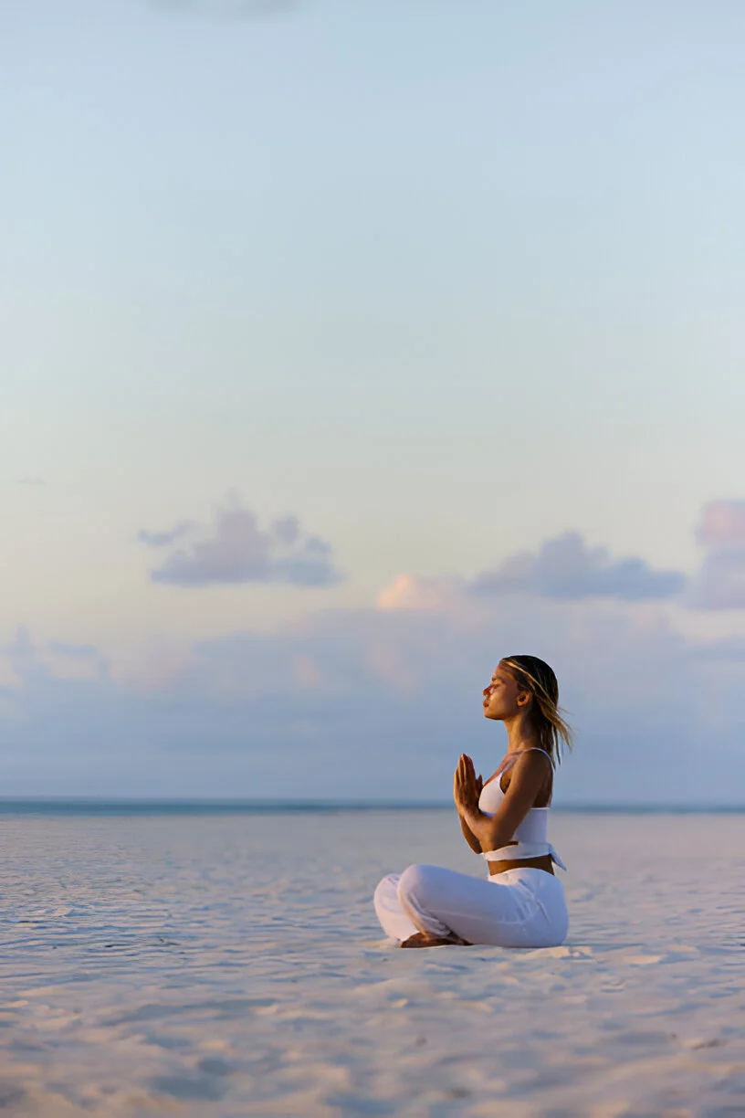 A woman sitting cross-legged on the beach, breathing calmly